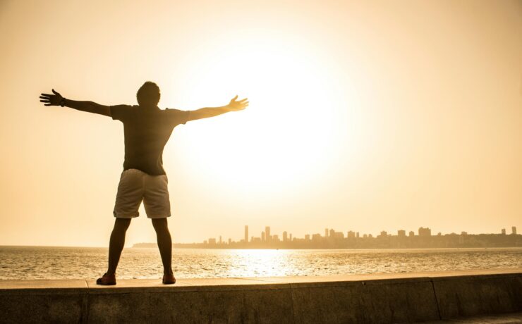 Man standing with arms open before the ocean, symbolizing freedom, surrender, and peace in recovery while working the Twelve Steps.