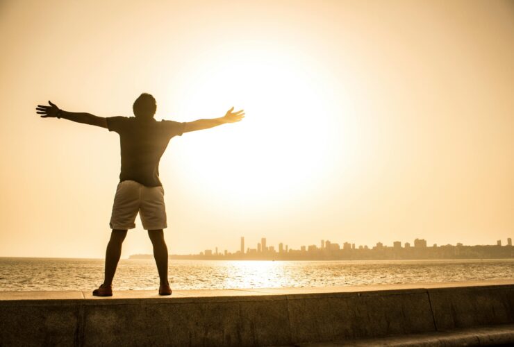 Man standing with arms open before the ocean, symbolizing freedom, surrender, and peace in recovery while working the Twelve Steps.